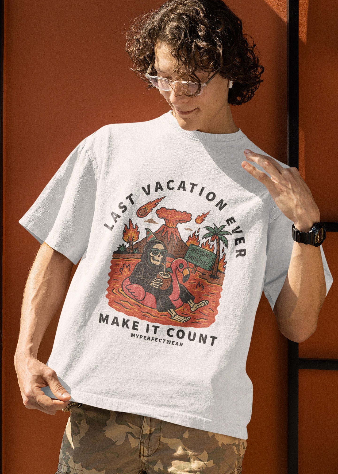 Person wearing a white t-shirt with a graphic design and text, standing against an orange wall.