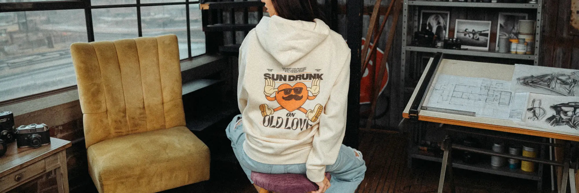 Woman in ecru boxy oversized hoodie with back print reading 'Sun Drunk on Old Love', heavyweight fleece