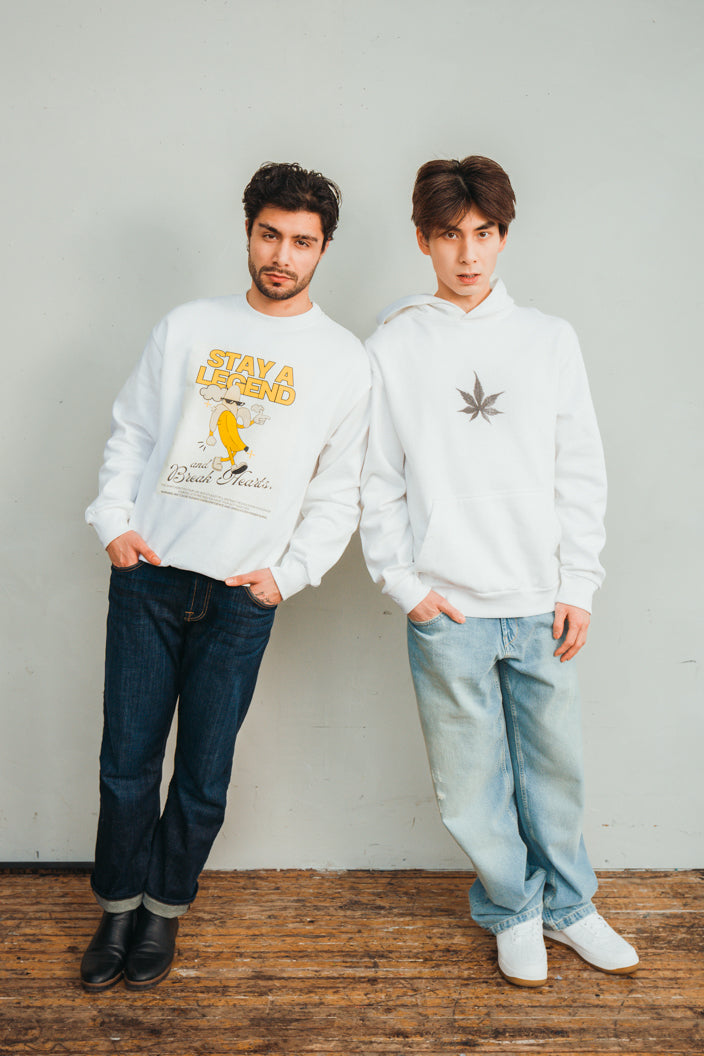 Man wearing white heavyweight  cotton graphic sweatshirt 'Stay a Legend' and man wearing graphic plant hoodie in front of wall