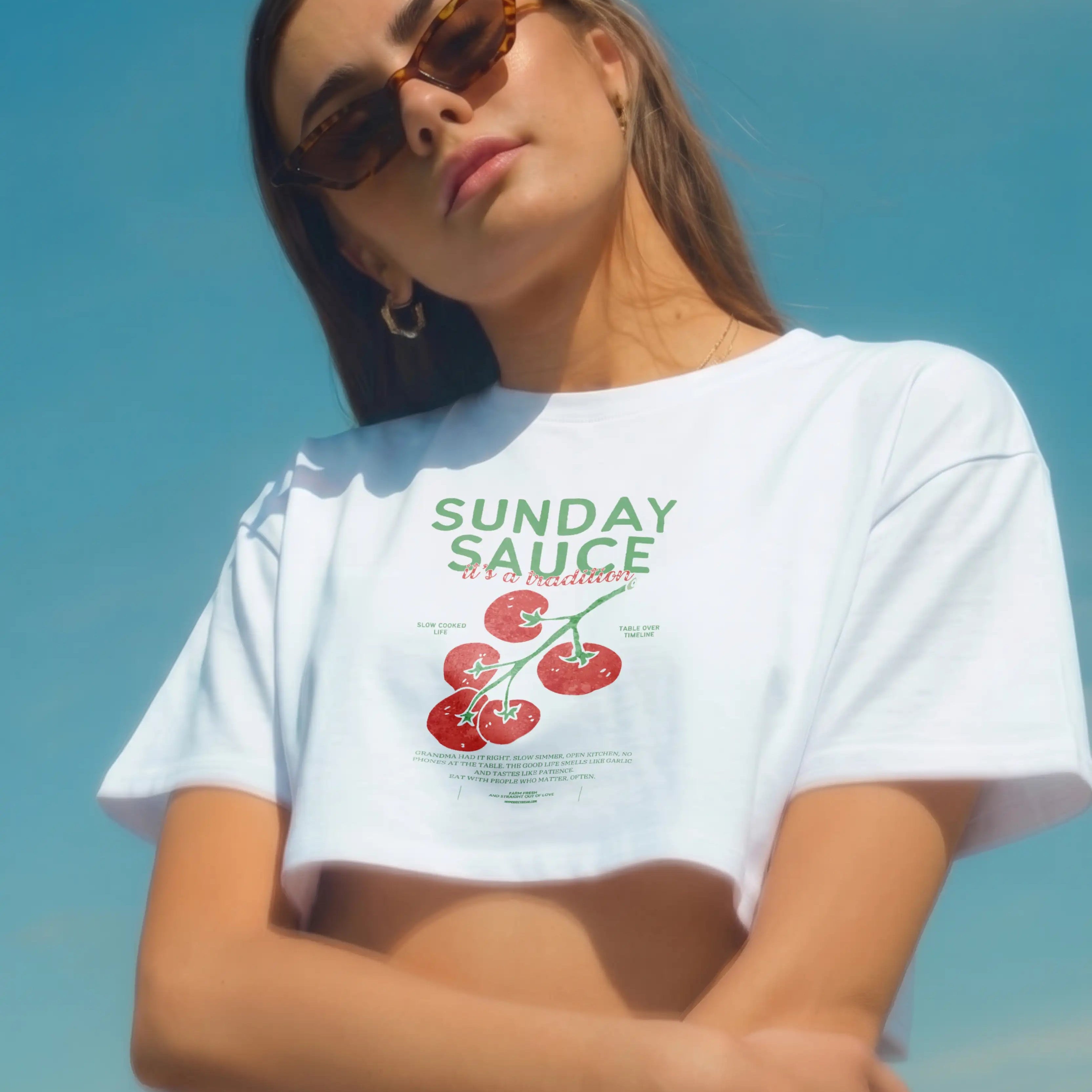 Woman wearing a white t-shirt with 'Sunday Sauce' graphic against a clear blue sky.