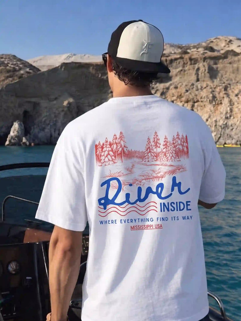 Person wearing a t-shirt with text "River Inside", standing on a boat with a natural landscape in the background.