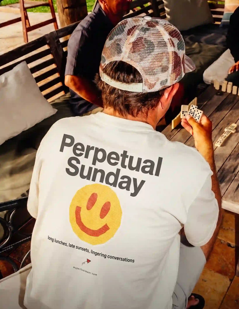 Person wearing a 'Perpetual Sunday' t-shirt with a smiley face, holding dice outdoors.
