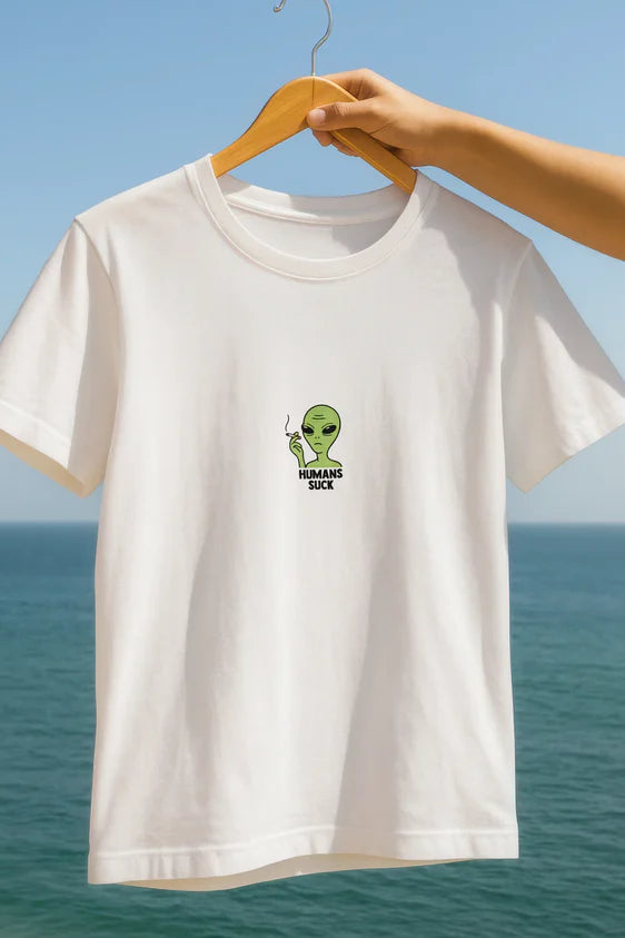 White t-shirt with alien graphic and text "Humans Suck", against a blue sky and ocean background